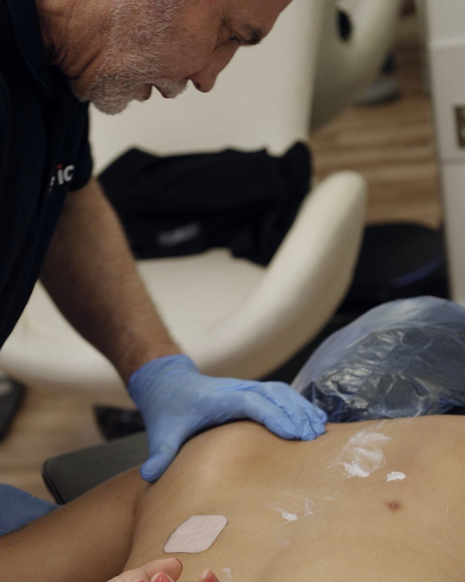 An MSK specialist's gloved hand working along the muscles beside a patient's spine.
