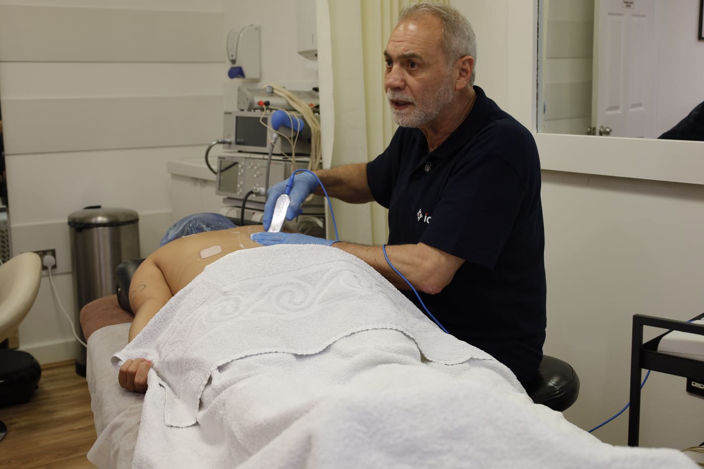 A clinician treating a patient lying on a treatment couch in the PRC Clinic treatment room.